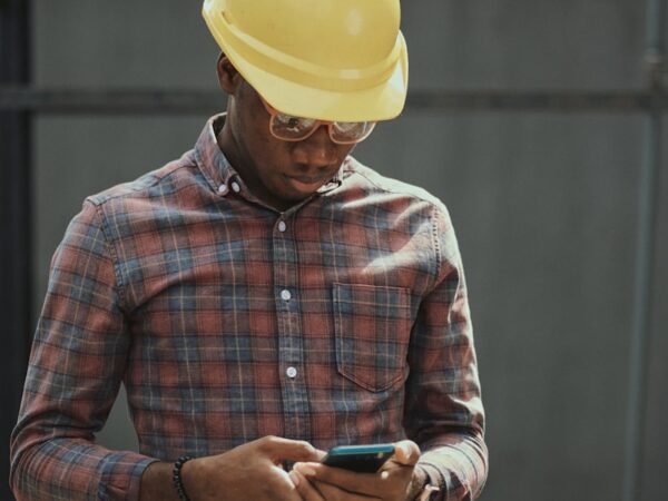 man in red blue and white plaid dress shirt wearing yellow hat holding black smartphone